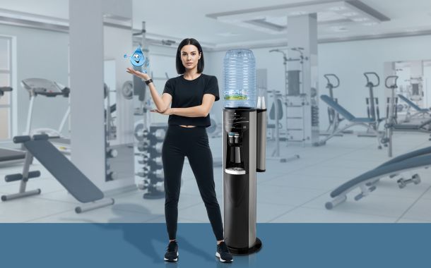 Donna in palestra con un erogatore di acqua Acquaviva, leader nella distribuzione di acqua in boccioni e erogatori a rete idrica, in un ambiente fitness e wellness